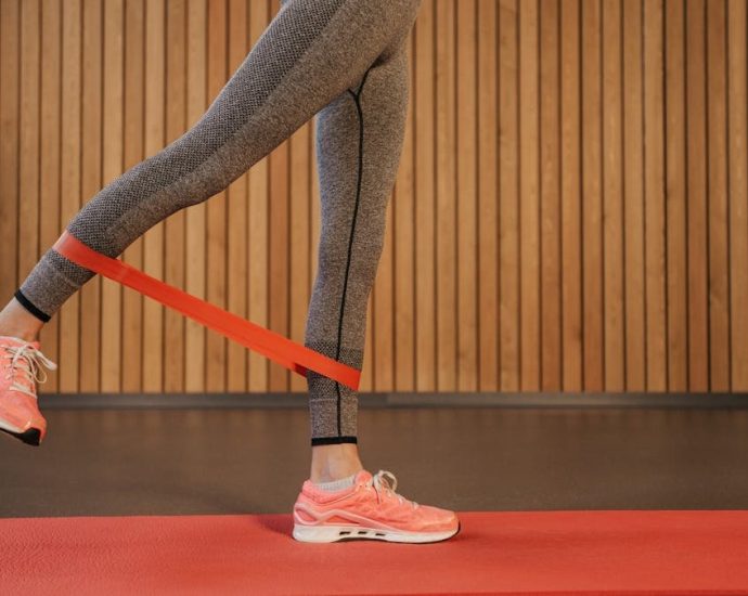 A woman performing leg exercises using a red resistance band on a yoga mat indoors.