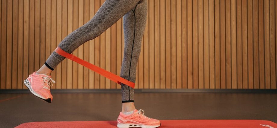 A woman performing leg exercises using a red resistance band on a yoga mat indoors.