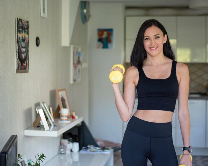 Smiling woman in activewear lifting dumbbells at home for a healthy lifestyle.