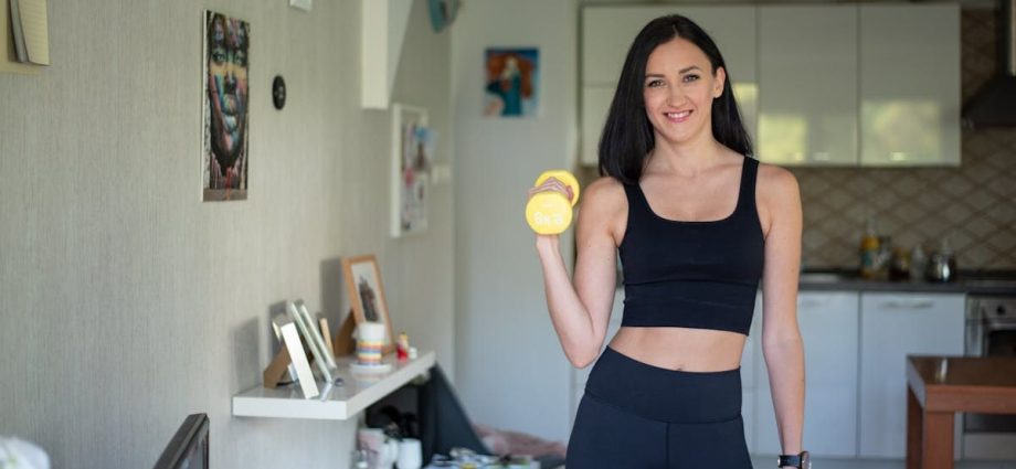 Smiling woman in activewear lifting dumbbells at home for a healthy lifestyle.